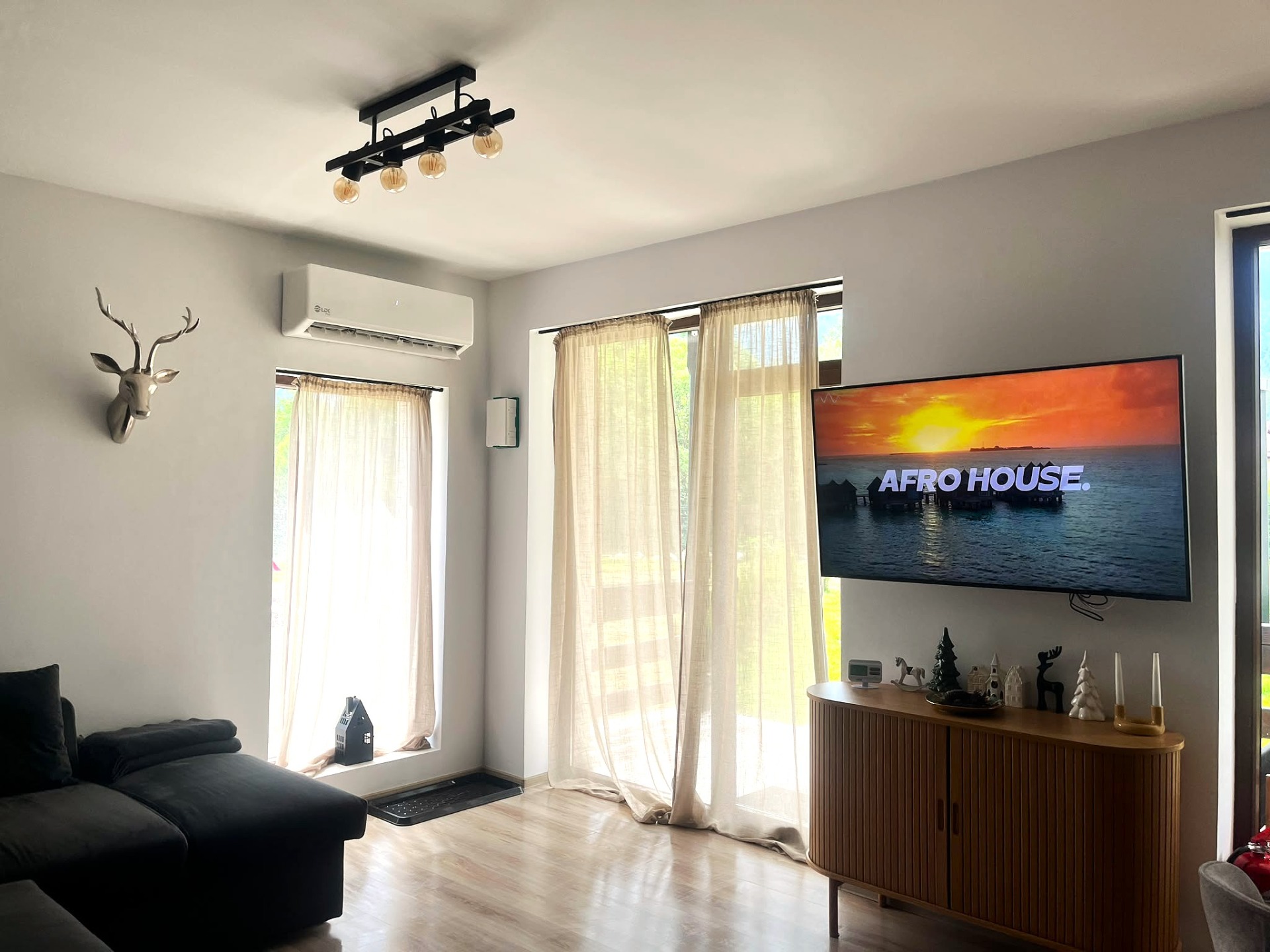 Living modern cu canapea, perdele bej, aparat de aer condiționat, televizor și veioze decorative pe mobilier; apartament in regim hotelier din Busteni, top 1% locuinte in Busteni